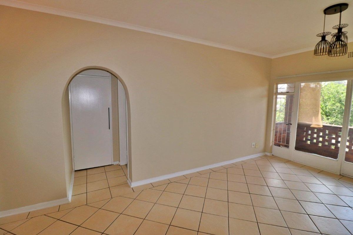 An empty living room featuring neutral tiled flooring, an arched doorway, and a sliding glass door providing access to an outdoor balcony area.