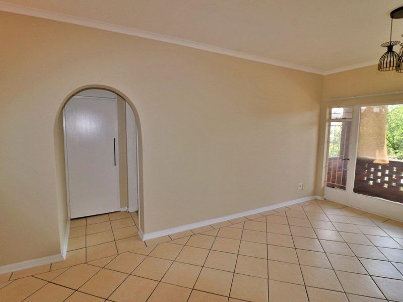 An empty living room featuring neutral tiled flooring, an arched doorway, and a sliding glass door providing access to an outdoor balcony area.