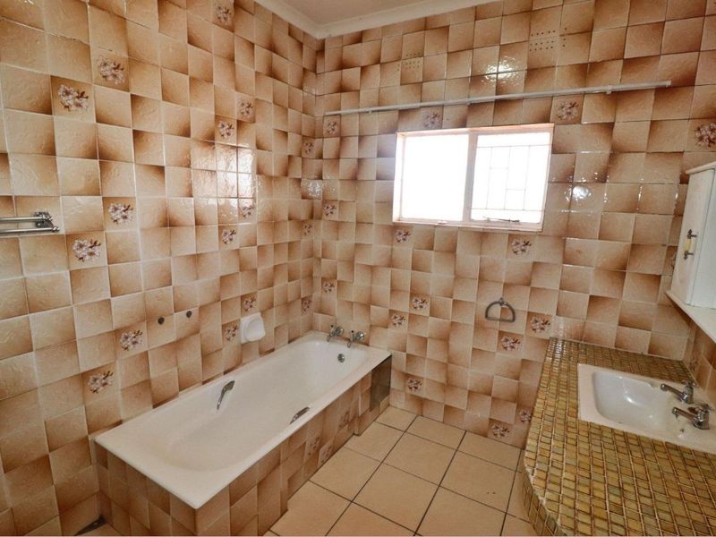 A dated bathroom featuring a built-in bathtub, tiled vanity with basin, and full-height wall tiling throughout.