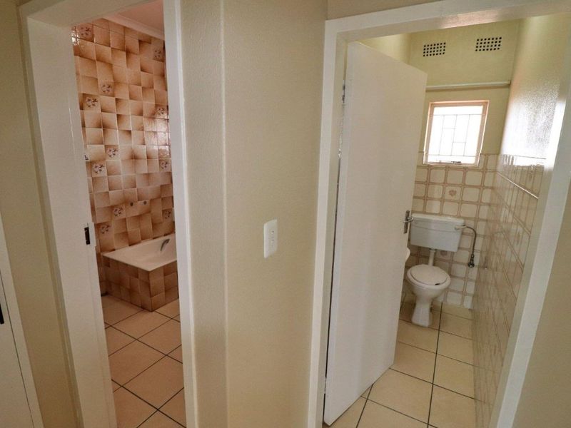 A functional bathroom layout featuring a separate bathtub area and a private toilet room with dated ceramic tile finishes.