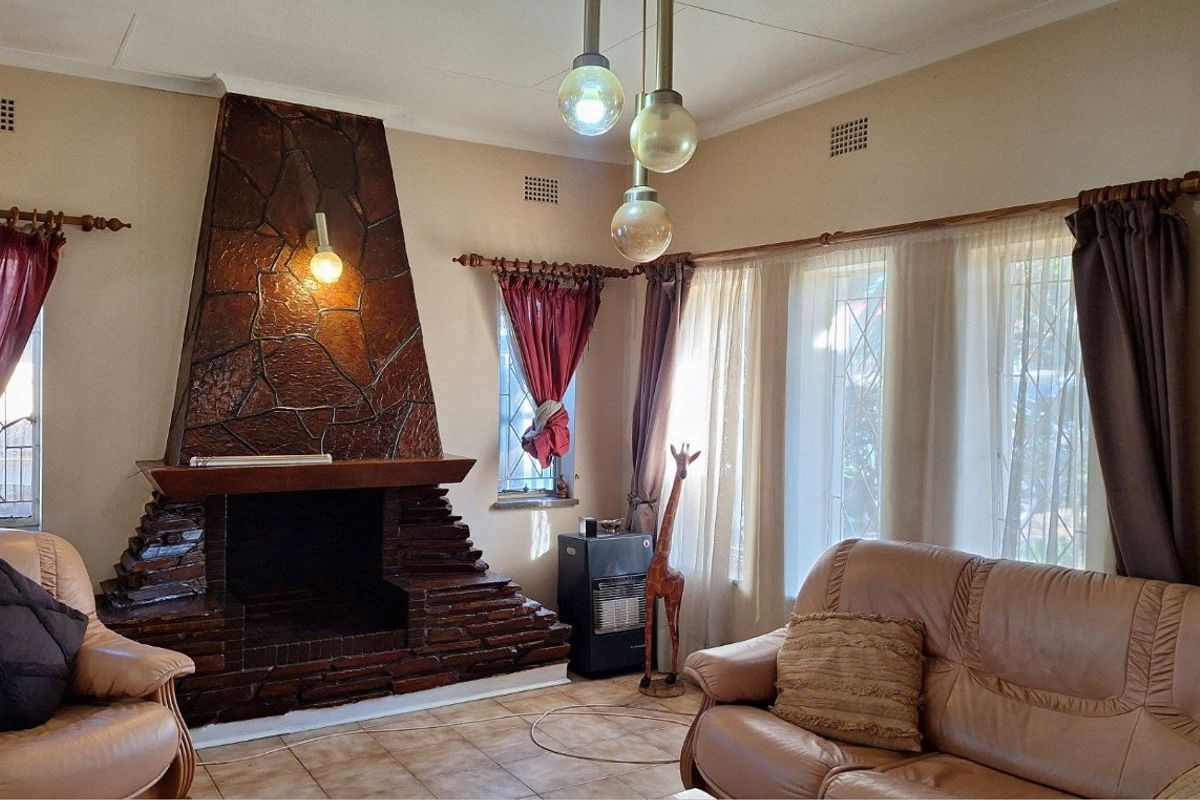 A living room featuring a prominent stone fireplace, tiled flooring, and large windows with leaded glass detailing.
