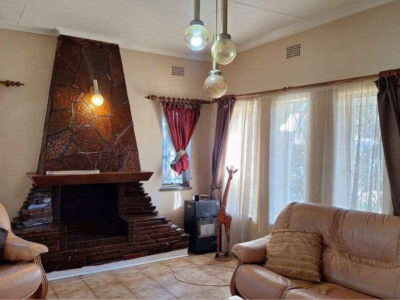 A living room featuring a prominent stone fireplace, tiled flooring, and large windows with leaded glass detailing.