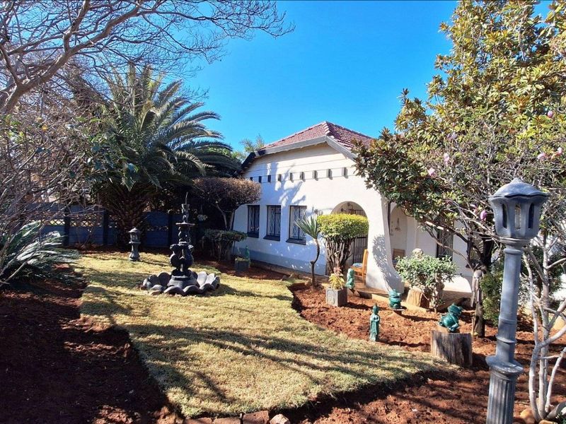 A view of the rear garden featuring a landscaped lawn, mature trees, a decorative fountain, and a classic house facade with an arched entrance.