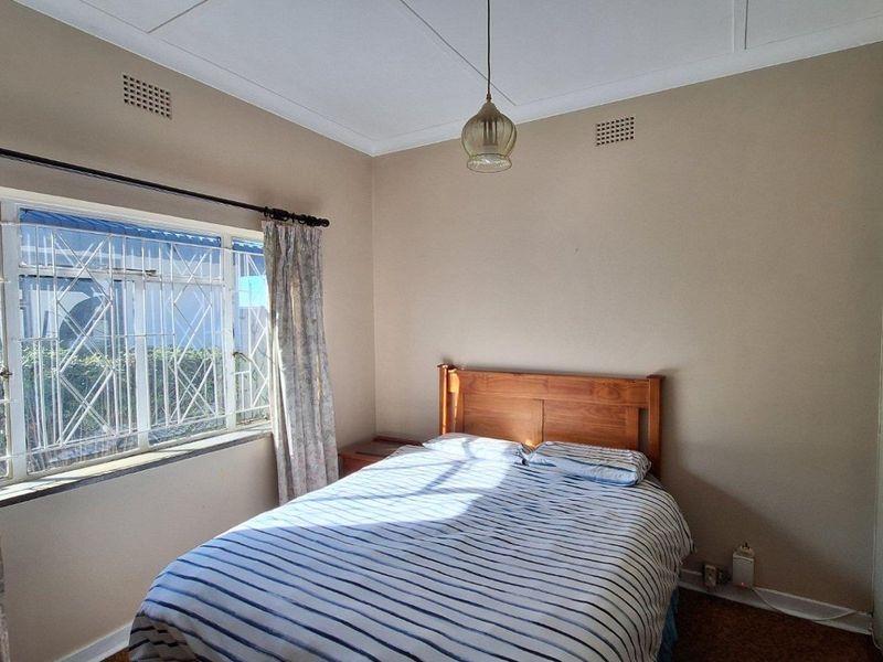 A standard bedroom featuring built-in cupboards, a steel window with security bars, and a central pendant light fixture.