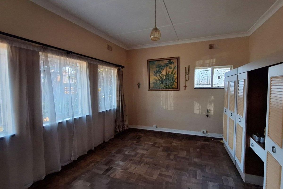 A bedroom featuring classic parquet flooring, coved cornicing, and built-in cupboards, with large windows fitted with security bars.