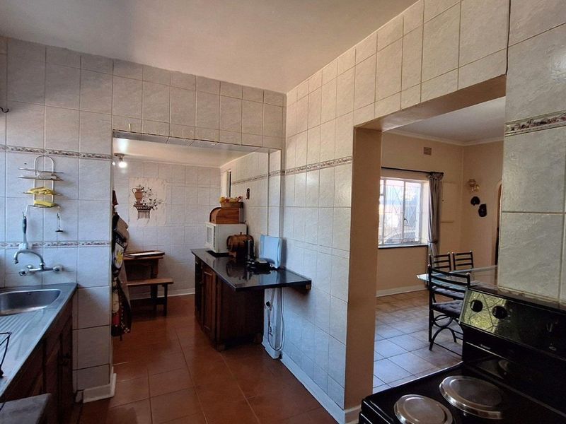 Functional kitchen featuring tiled walls, built-in cabinetry, and a stainless steel sink, with an open-plan layout connecting to the adjacent dining area.