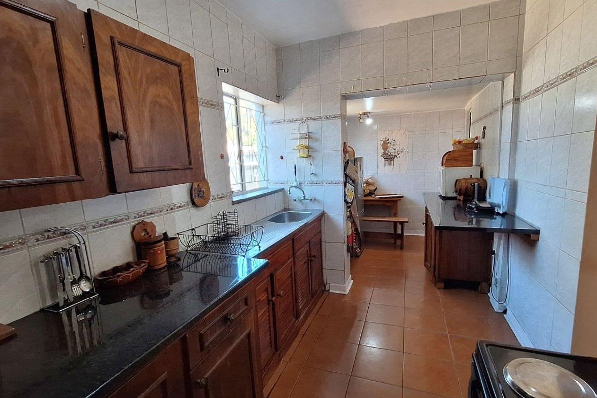 A functional kitchen featuring dark wood cabinetry, granite countertops, tiled walls, and tiled flooring, with an adjacent secondary prep or dining area.
