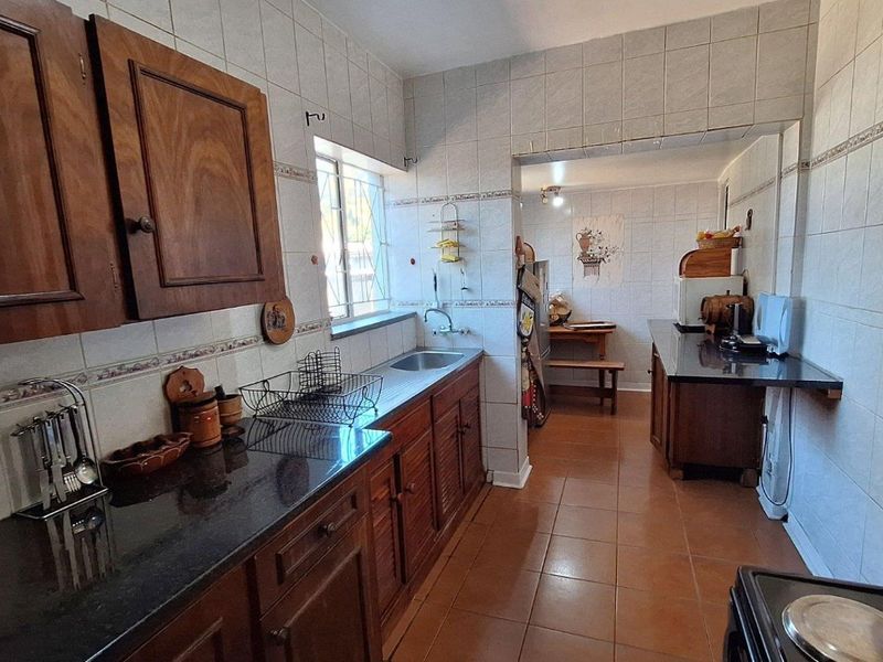 A functional kitchen featuring dark wood cabinetry, granite countertops, tiled walls, and tiled flooring, with an adjacent secondary prep or dining area.