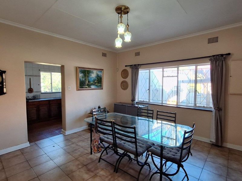 A dining room featuring tiled flooring, large windows with security bars, and an open archway leading into the kitchen area.
