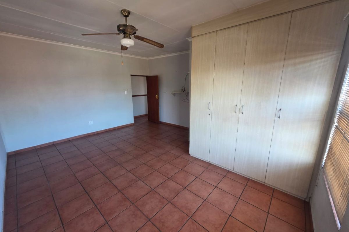 Spacious bedroom featuring tiled flooring, built-in cupboards, and a ceiling fan, offering a clean and functional space ready for personalization.