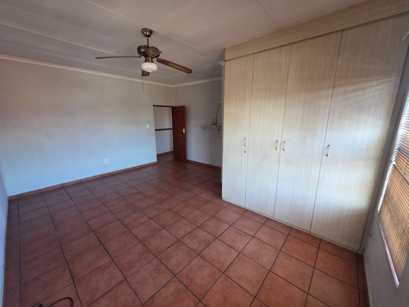 Spacious bedroom featuring tiled flooring, built-in cupboards, and a ceiling fan, offering a clean and functional space ready for personalization.