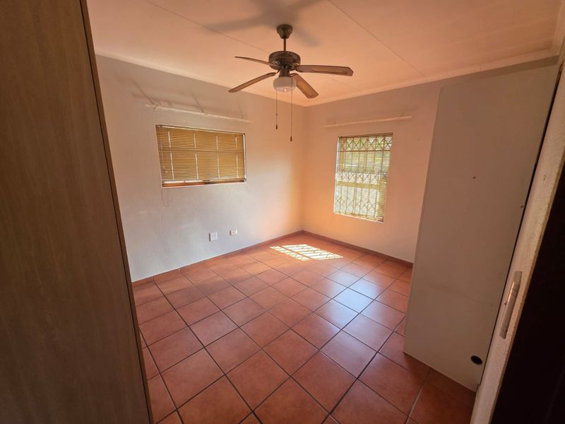 A bright, empty bedroom featuring tiled flooring, a ceiling fan, and security bars on the windows, offering a clean canvas for personalization.