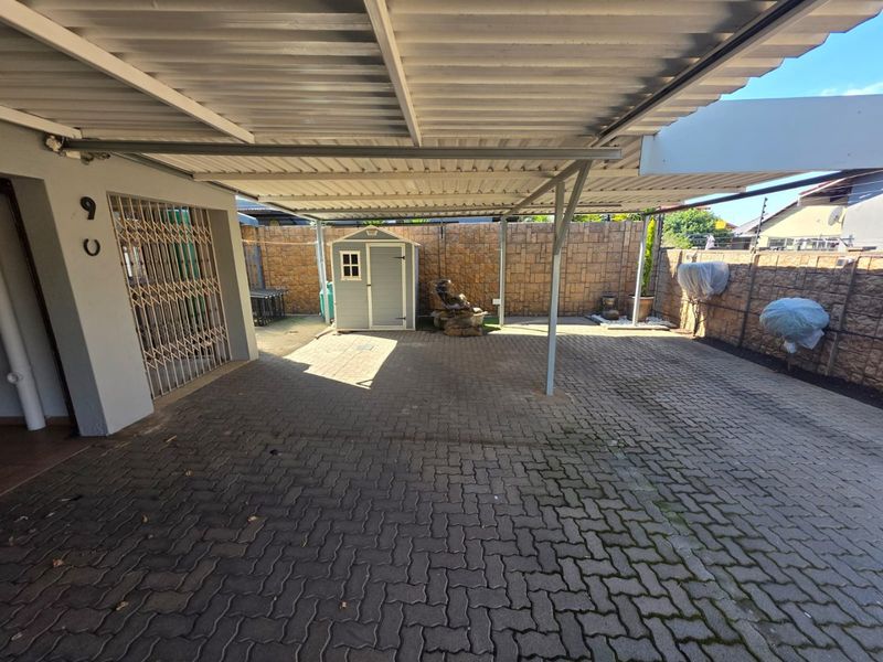 A covered carport area featuring paved flooring, a secure metal gate, and perimeter boundary walls.