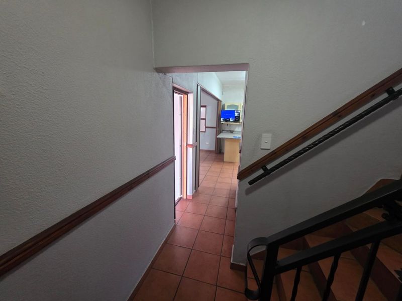 A functional hallway featuring tiled flooring and a staircase with a wrought iron balustrade, providing access to the kitchen area.