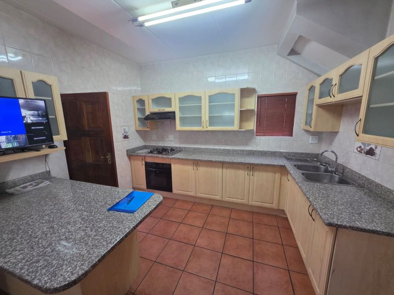 A functional kitchen featuring granite countertops, wooden cabinetry, a built-in oven with gas hob, and tiled flooring throughout.