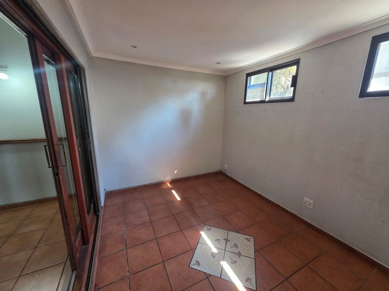 An empty, sunlit living area featuring terracotta tiled flooring, sliding glass doors, and aluminium-framed windows, offering a blank canvas for interior design.