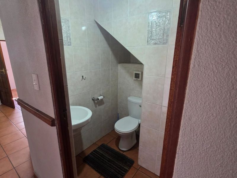 A compact guest bathroom featuring a pedestal sink, toilet, and neutral ceramic tiling, situated under a staircase.
