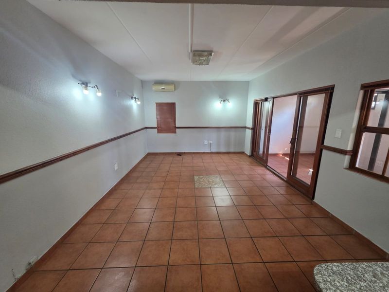 Spacious living area featuring terracotta floor tiles, wooden sliding doors leading to an outdoor space, and a wall-mounted air conditioning unit.