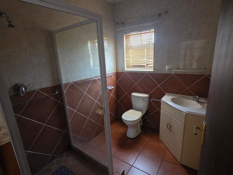 A functional bathroom featuring a shower enclosure, toilet, and vanity cabinet with a washbasin, finished with tiled walls and flooring.