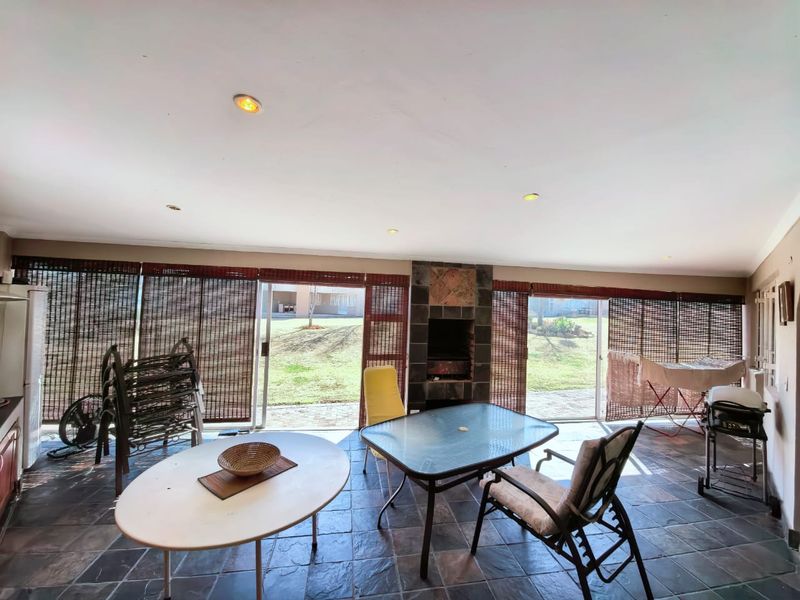 A spacious covered patio featuring tiled flooring, a built-in braai, and large sliding glass doors that open to the garden.