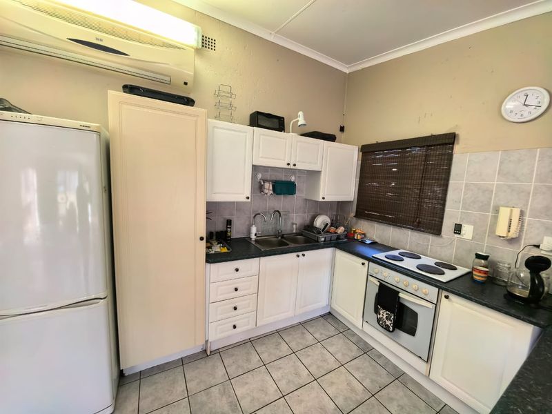 A functional kitchen featuring white cabinetry, a double sink, an electric hob with oven, and tiled flooring, complemented by a wall-mounted air conditioning unit.