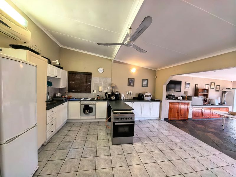 Spacious open-plan kitchen and living area featuring tiled flooring, built-in cabinetry, and a central oven, offering a functional layout with potential for modern updates.