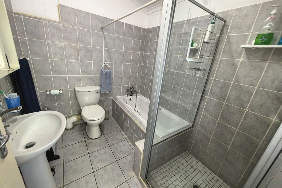 Functional bathroom featuring a pedestal basin, toilet, built-in bathtub, and a separate shower enclosure with grey ceramic tiling throughout.