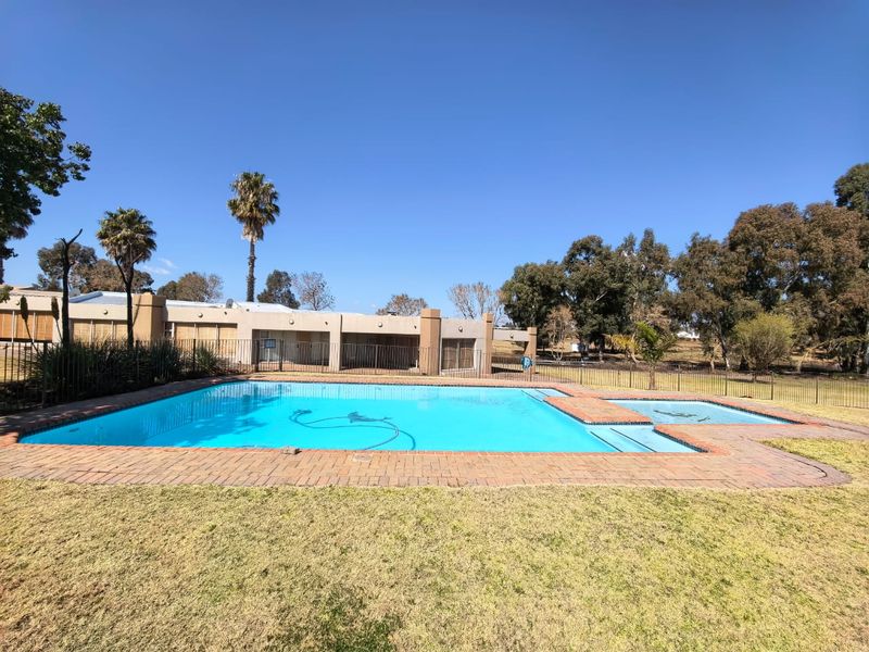 Outdoor swimming pool area featuring an integrated spa, brick coping, and metal perimeter fencing set within a spacious garden.