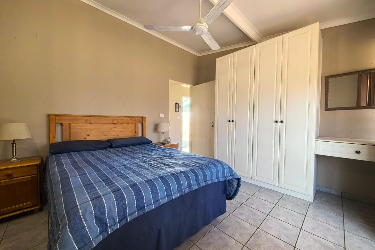 A functional bedroom featuring tiled flooring, a ceiling fan, and ample built-in wardrobe storage with an integrated vanity area.