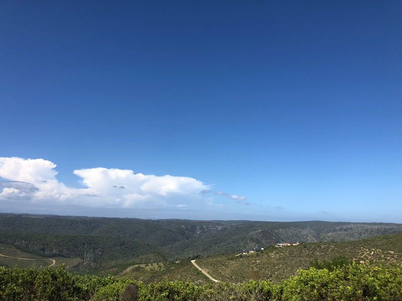 A scenic elevated view overlooking rolling hills, native vegetation, and distant landscape under a clear blue sky.