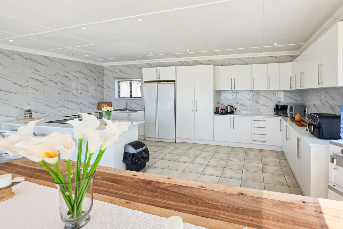 Modern kitchen featuring white cabinetry, marble-look wall tiles, a central island, and integrated appliances, offering a clean and functional culinary space.