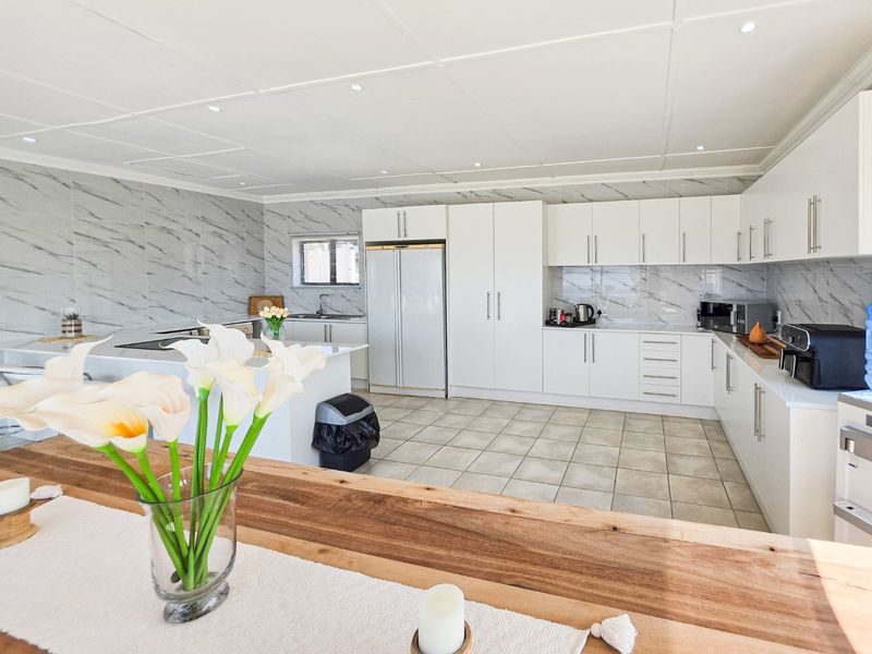 Modern kitchen featuring white cabinetry, marble-look wall tiles, a central island, and integrated appliances, offering a clean and functional culinary space.
