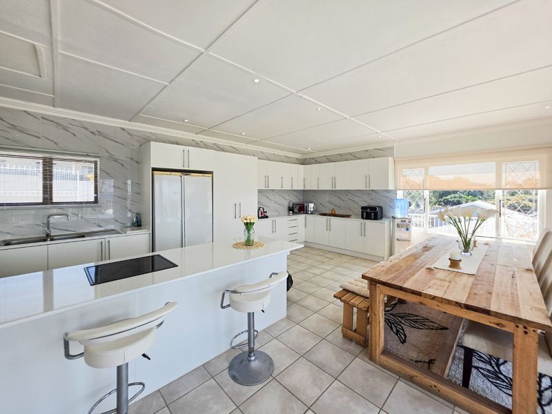 Spacious open-plan kitchen and dining area featuring modern white cabinetry, stone countertops, a central island with a cooktop, and large windows for natural light.