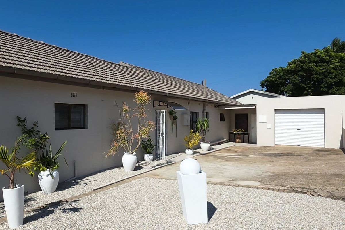 Rear exterior view of the house featuring a tiled roof, concrete driveway, and attached garage with gravel landscaping.