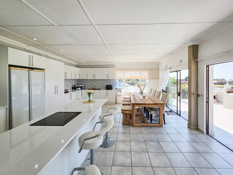 Spacious open-plan kitchen and dining area featuring modern white cabinetry, stone countertops, a central island, and seamless access to an outdoor patio.
