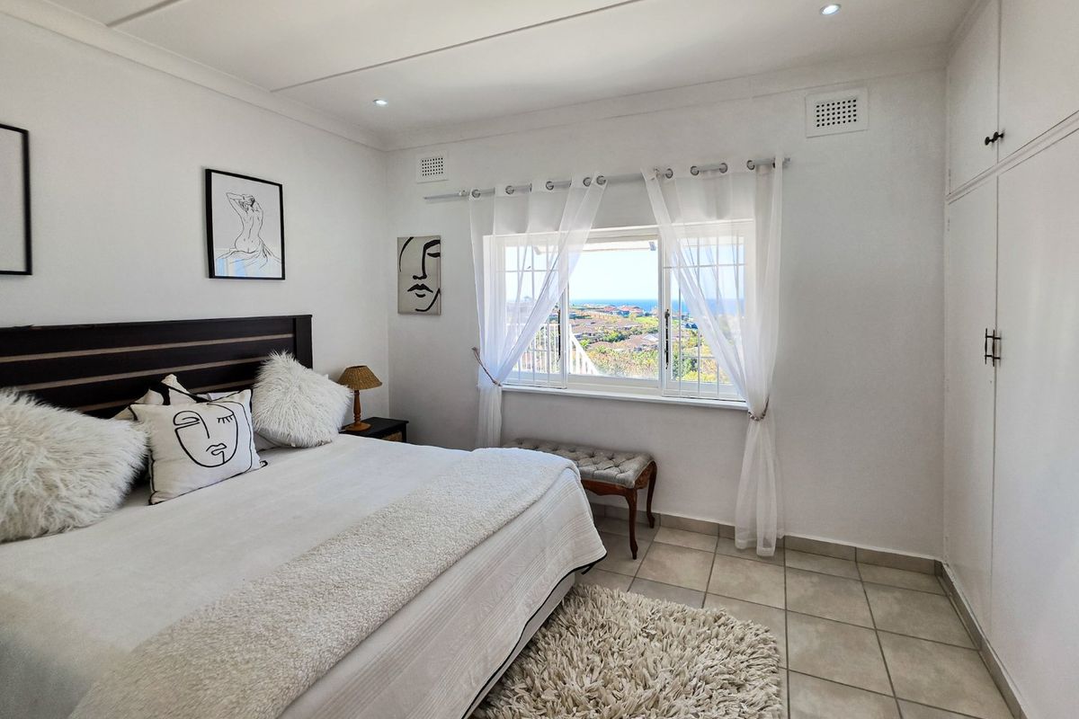 A bright bedroom featuring tiled flooring, built-in cupboards, and a window offering scenic coastal views.
