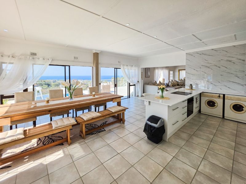 Spacious open-plan living and kitchen area featuring a marble-look island, tiled floors, and large sliding doors opening to a scenic coastal view.
