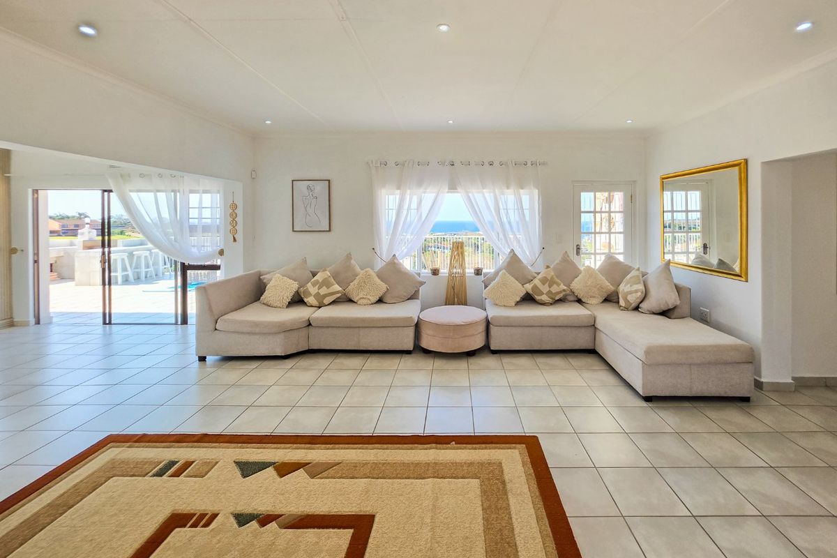 Spacious living room featuring neutral tiled flooring, recessed lighting, and large windows with ocean views, providing seamless access to the outdoor patio area.