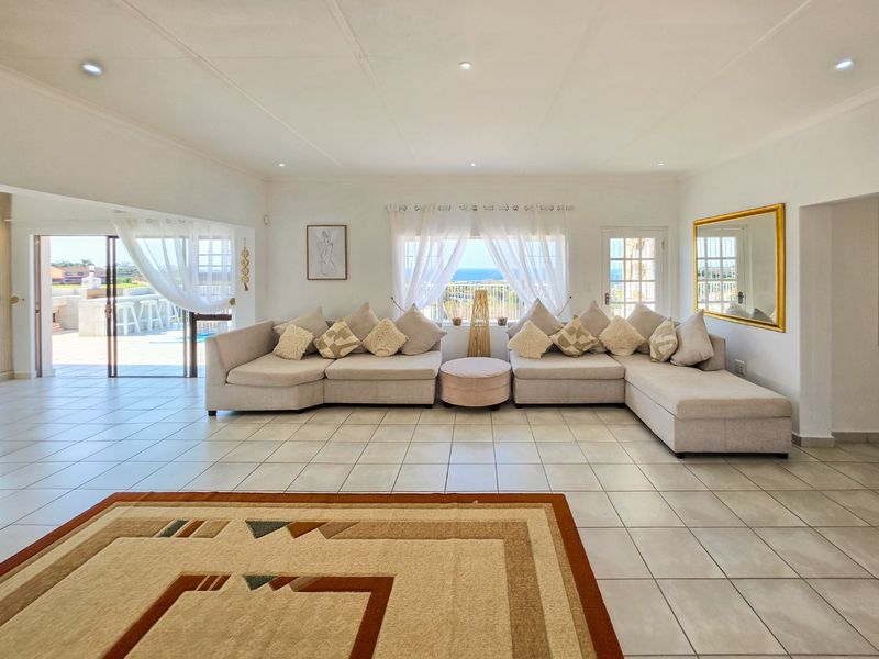 Spacious living room featuring neutral tiled flooring, recessed lighting, and large windows with ocean views, providing seamless access to the outdoor patio area.