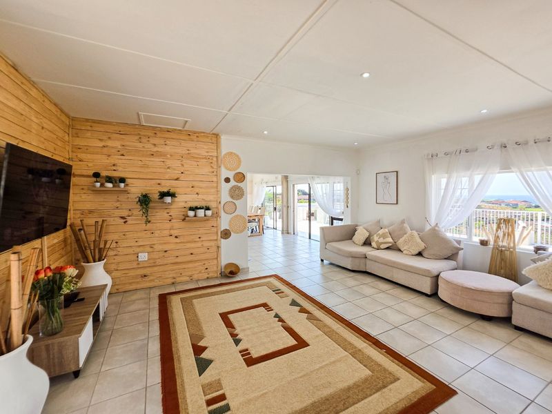 Spacious open-plan living area featuring timber wall cladding, tiled flooring, and seamless access to an adjoining patio through sliding glass doors.