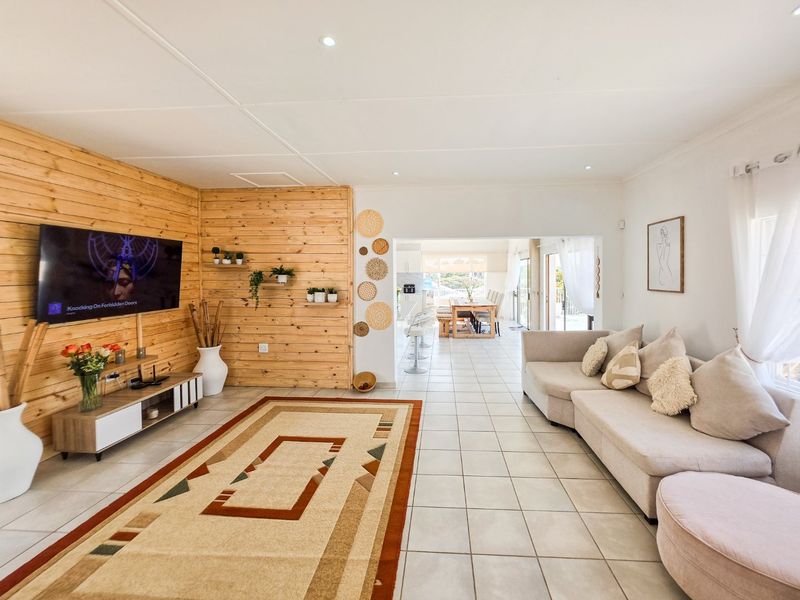 Spacious open-plan living area featuring modern tiled flooring, recessed downlights, and a warm timber-clad feature wall, flowing seamlessly into the dining and kitchen space.