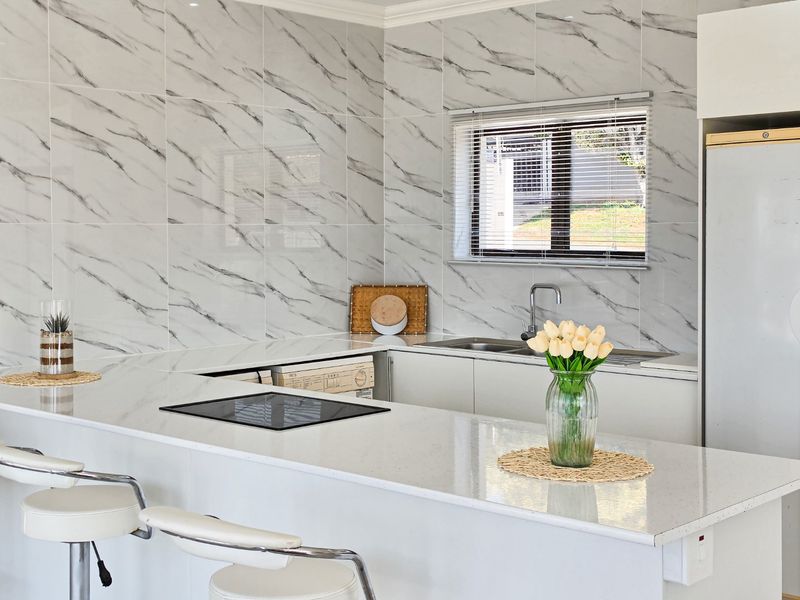 Modern kitchen featuring marble-look wall tiling, a spacious quartz breakfast bar, integrated induction hob, and a clean, minimalist aesthetic.