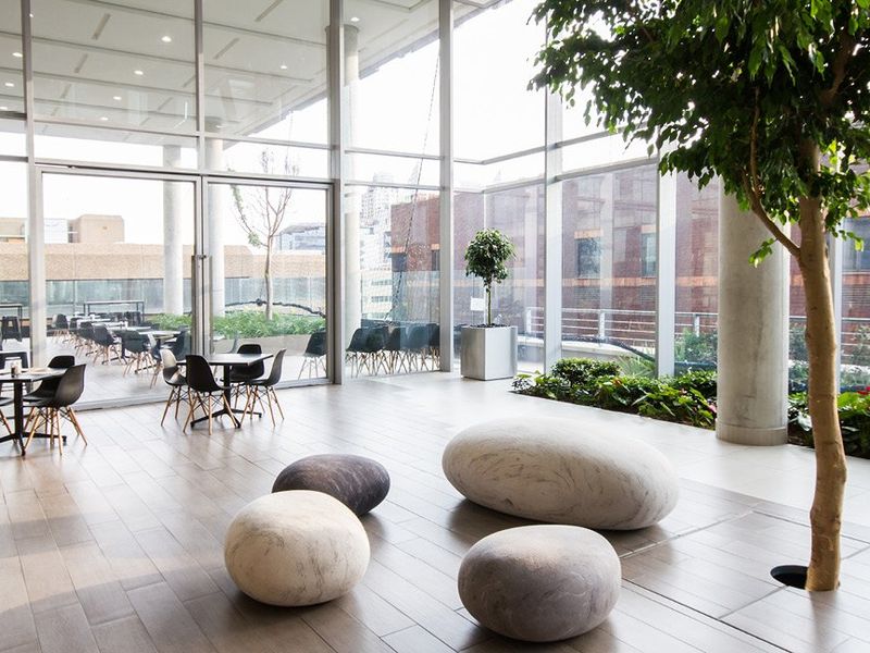 Modern open-plan commercial space featuring floor-to-ceiling glass walls, tiled flooring, concrete columns, and an integrated indoor garden area with seamless outdoor access.
