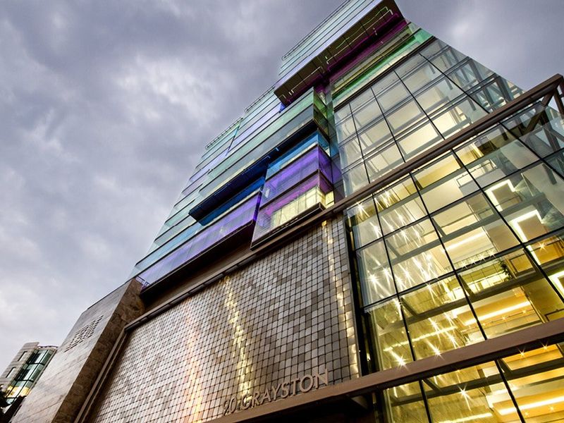 Modern commercial office building facade featuring a striking glass curtain wall, decorative tiled exterior, and integrated architectural lighting.