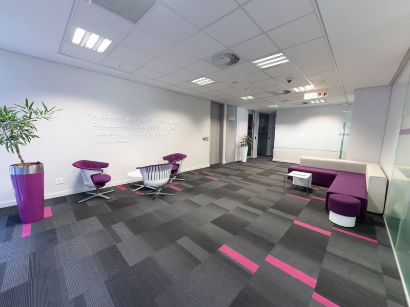A modern commercial office reception or breakout area featuring carpet tiles, suspended ceilings, and glass partitioning.