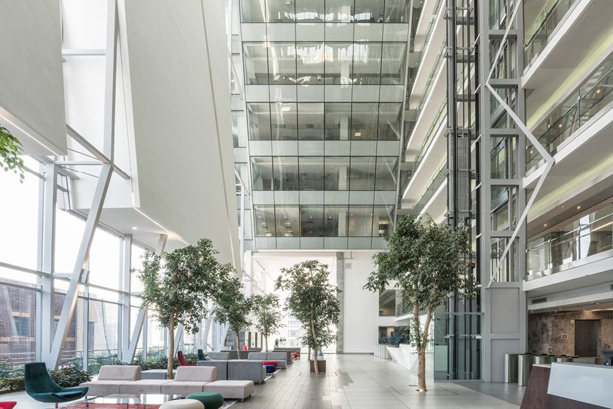 Spacious modern commercial atrium featuring a glass curtain wall, high ceilings, and a prominent glass elevator shaft in a professional office building.