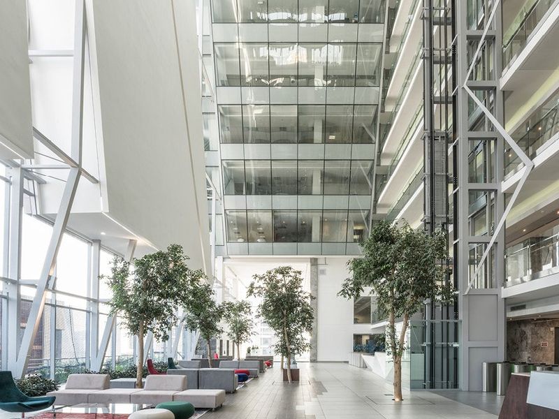 Spacious modern commercial atrium featuring a glass curtain wall, high ceilings, and a prominent glass elevator shaft in a professional office building.