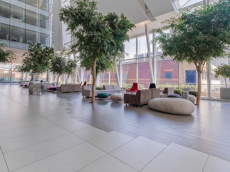 Spacious commercial atrium featuring high ceilings, extensive glass curtain walls, indoor trees, and modern porcelain tile flooring in a bright, professional lobby setting.