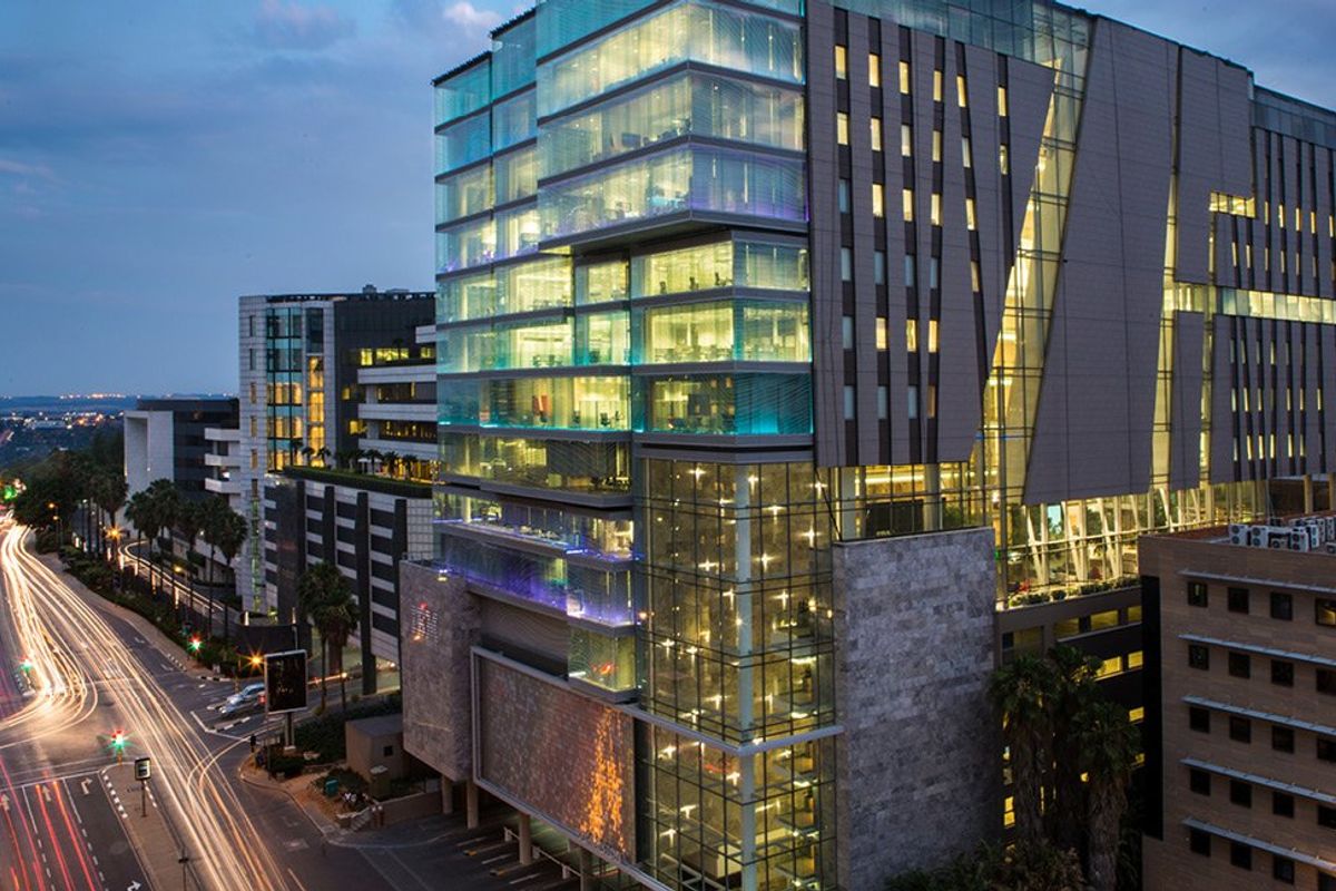 Aerial view of a modern commercial office building at dusk, featuring extensive glass curtain walling, stone facade elements, and integrated architectural lighting.