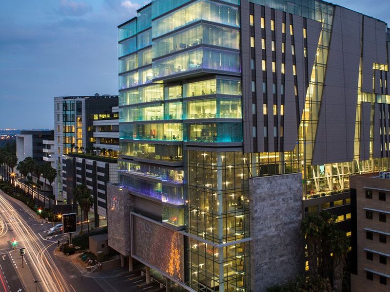 Aerial view of a modern commercial office building at dusk, featuring extensive glass curtain walling, stone facade elements, and integrated architectural lighting.
